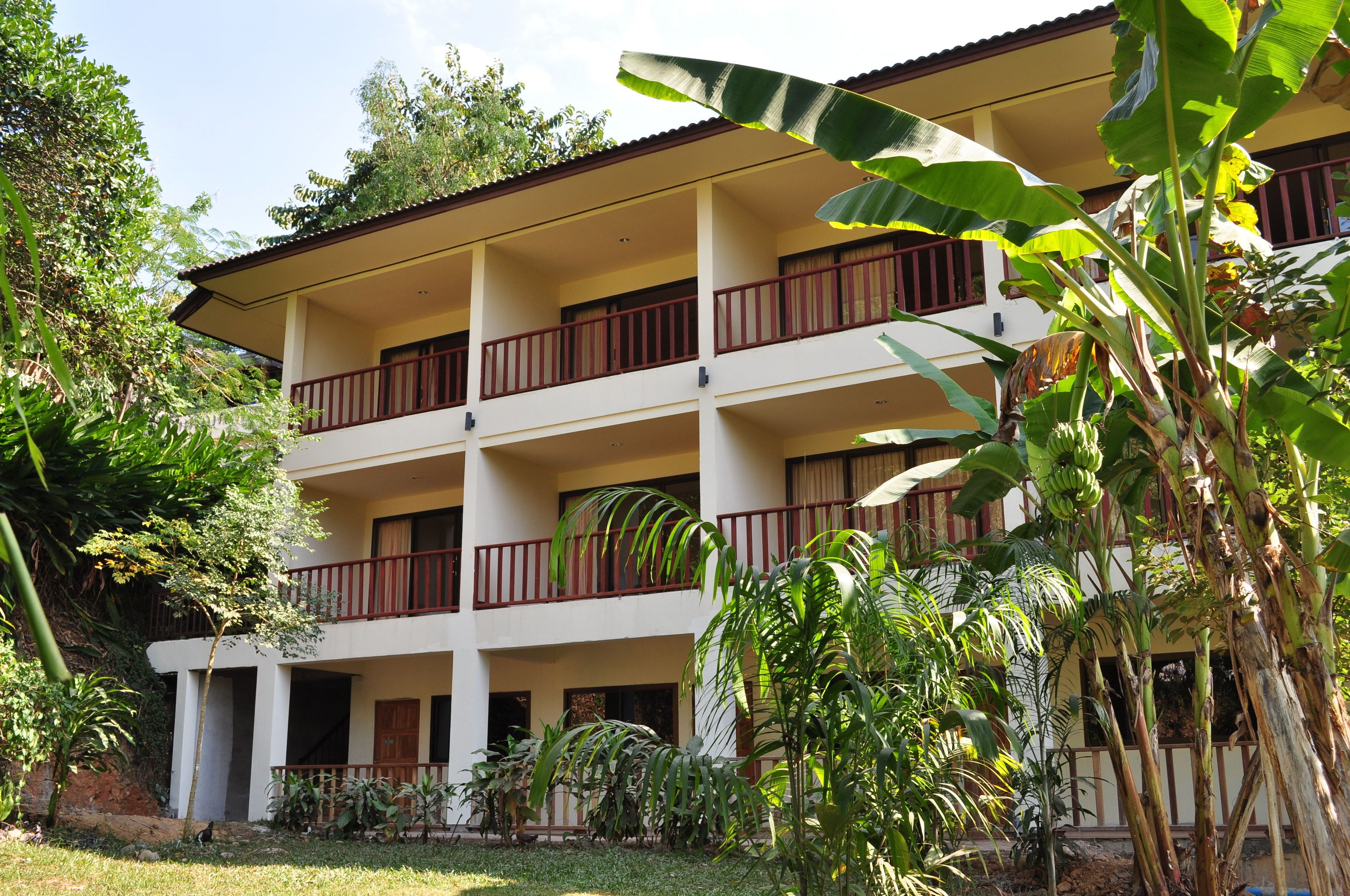 Un edificio de varios pisos con balcones, rodeado de abundante vegetación y palmeras de banano.