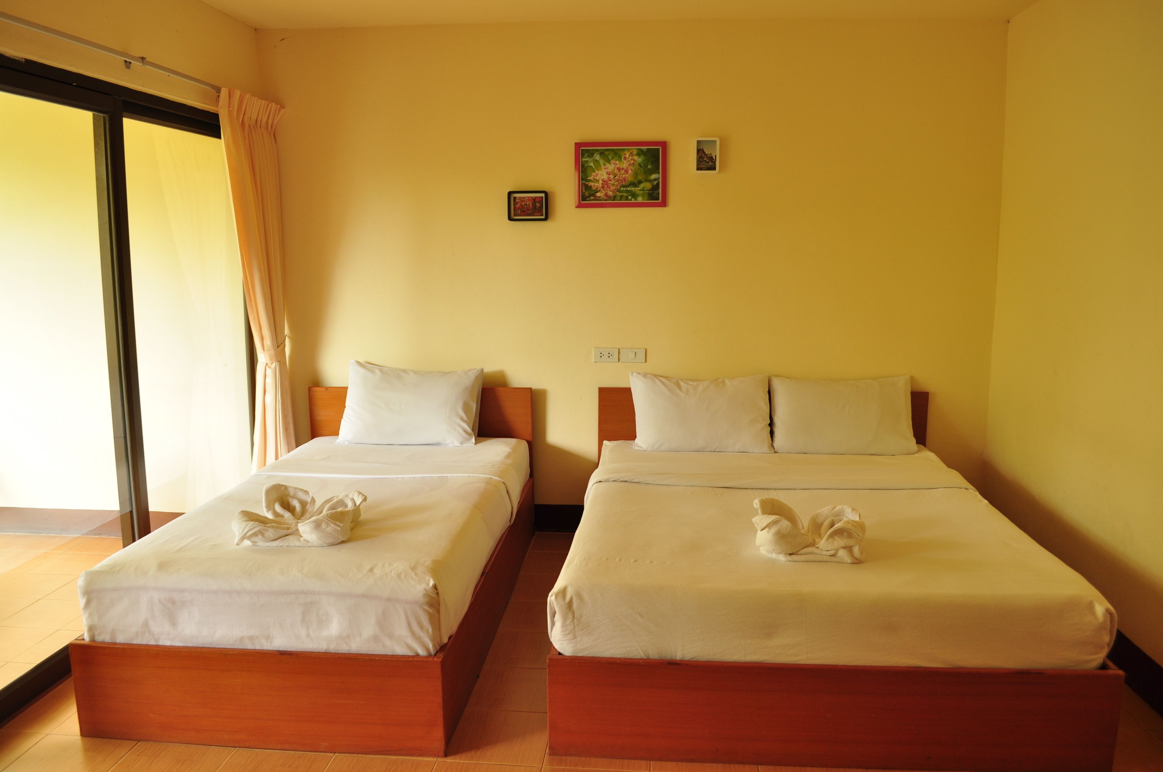 A hotel room with two beds, a large window with curtains, and a wall with two small framed pictures.