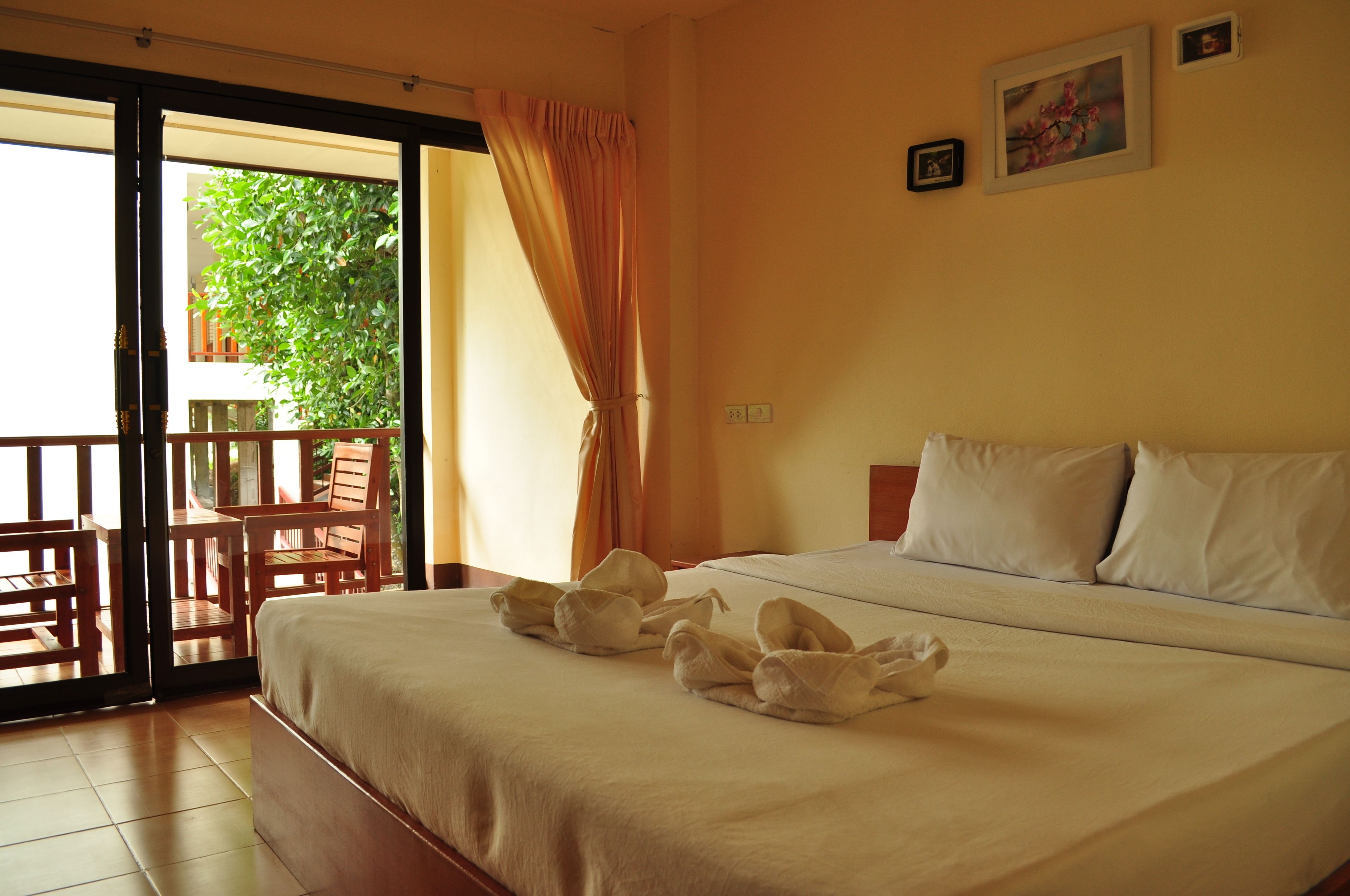 Quarto de hotel com uma cama, varanda com mobiliário de madeira e vista para o verde lá fora.