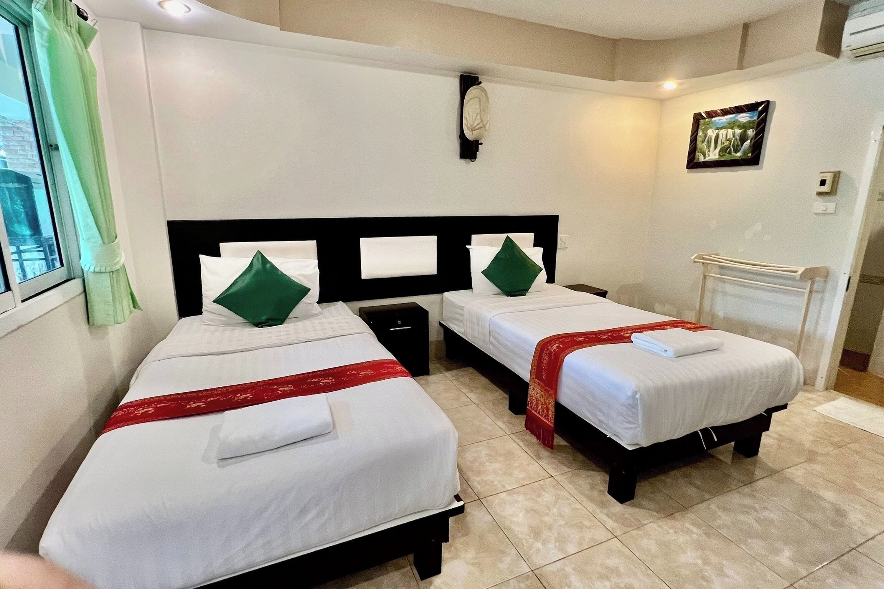Habitación de hotel con dos camas individuales, cada una con cubrecama rojo y verde, cabecero blanco y mesita de noche.