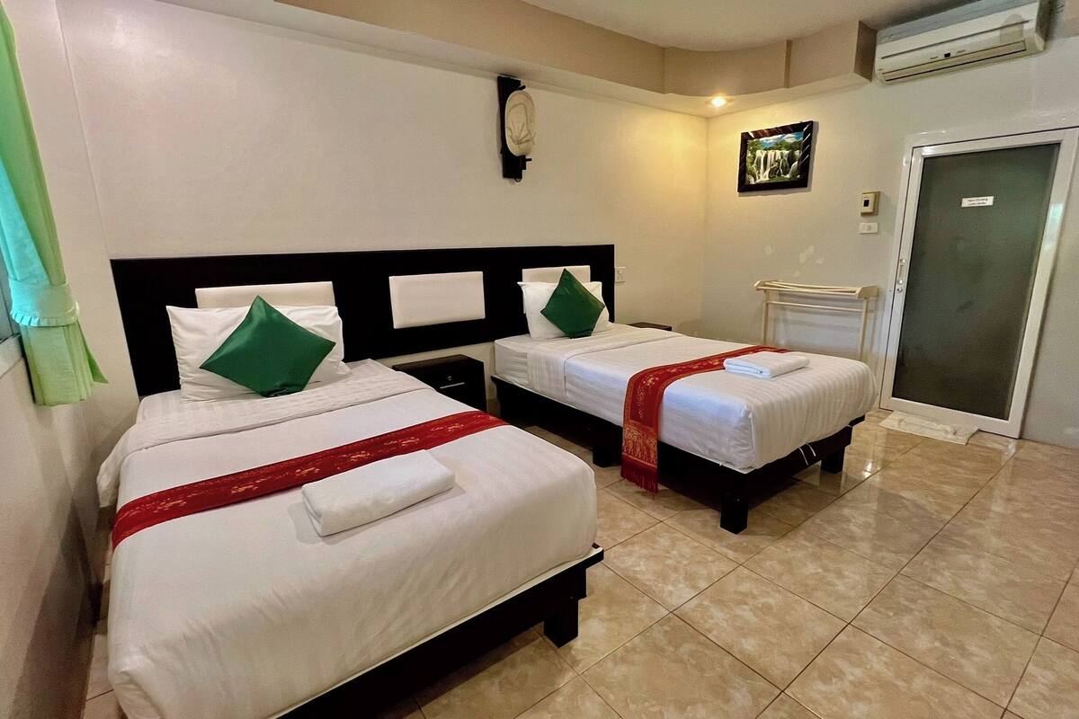 A hotel room with two beds, each with white bedding and green pillows, a red bedspread, and a white wall clock.