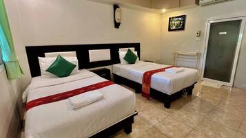 A hotel room with two beds, each with white bedding and green pillows, a red bedspread, and a white wall clock.