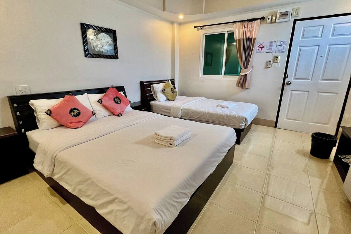 A hotel room with two beds, a window with curtains, a door, and a wall-mounted air conditioning unit.