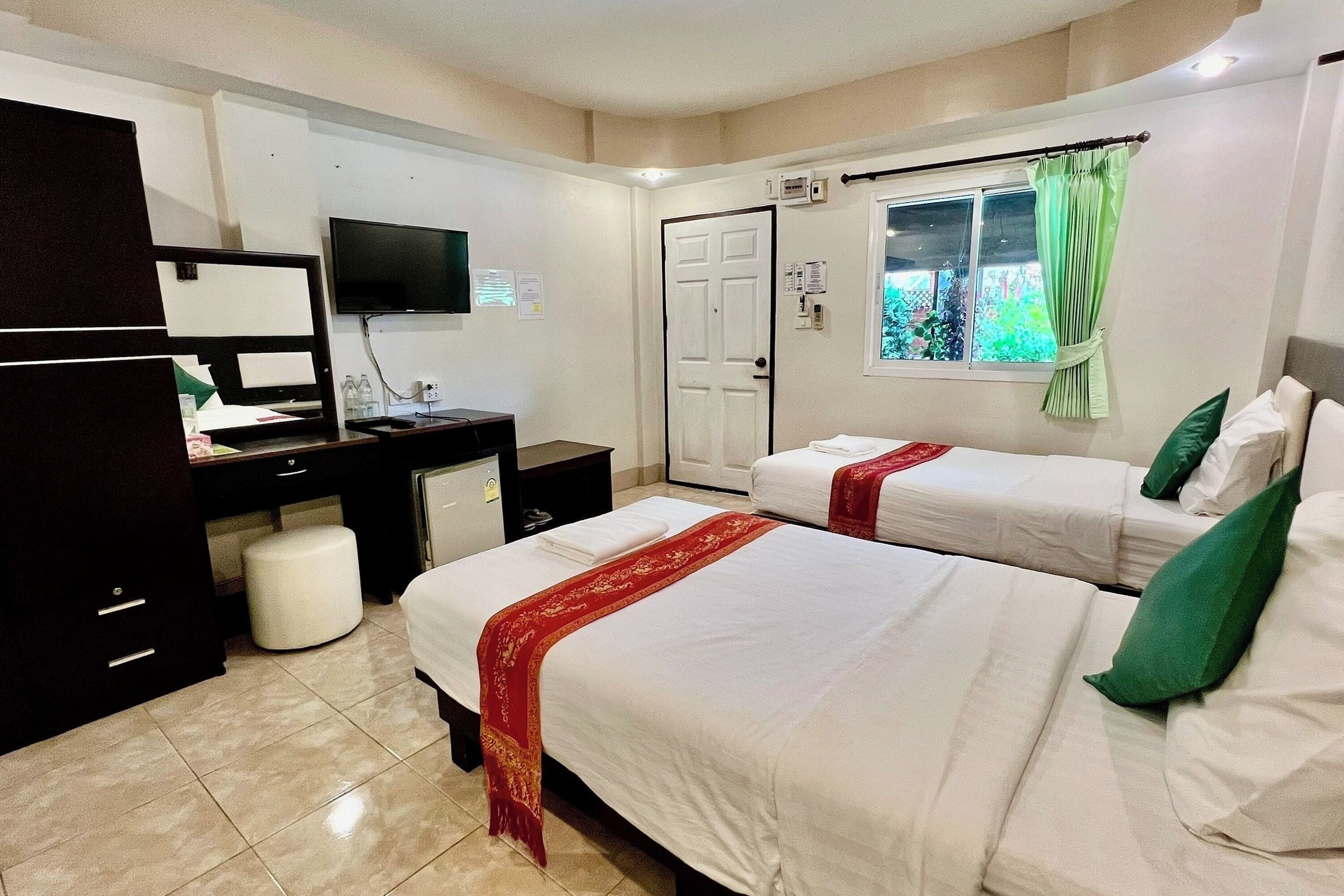 A hotel room with two beds, a desk, a television, and a window with curtains.