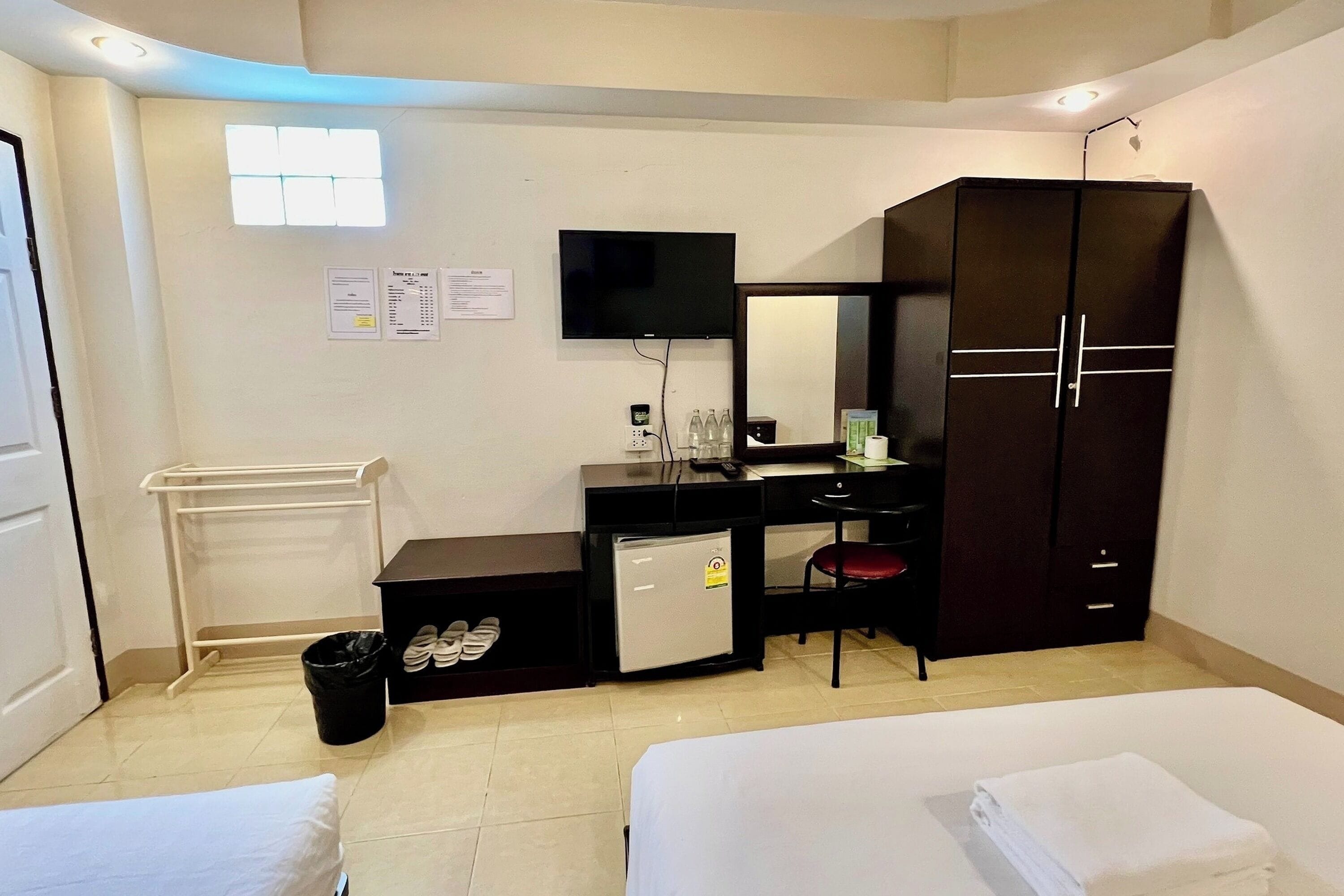 A hotel room with a bed, a desk with a computer, a TV, a wardrobe, and a small fridge.