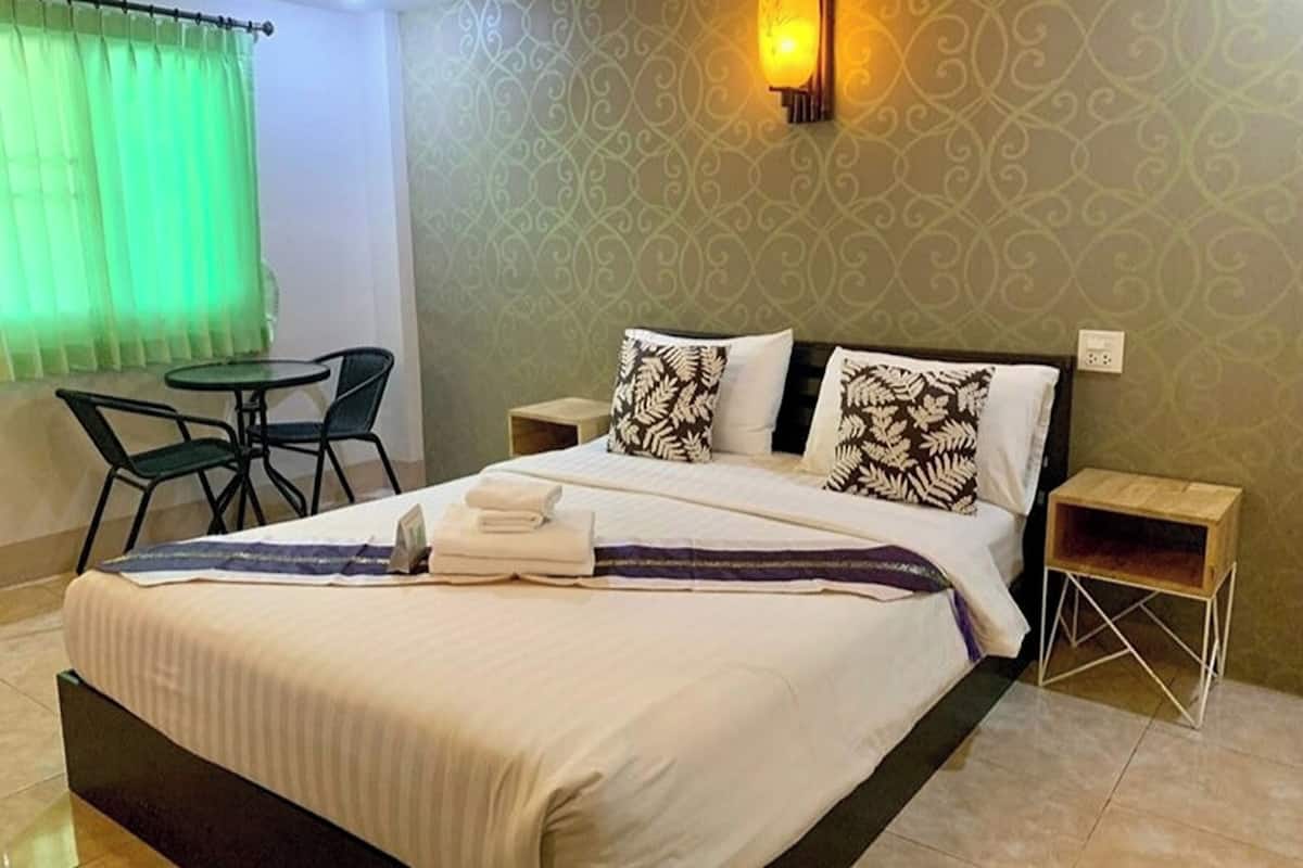 A neatly made bed with a white and black patterned pillow, a small bedside table, and a green chair.