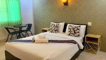 Cama bem arrumada com travesseiro estampado em preto e branco, uma pequena mesa de cabeceira e uma cadeira verde.