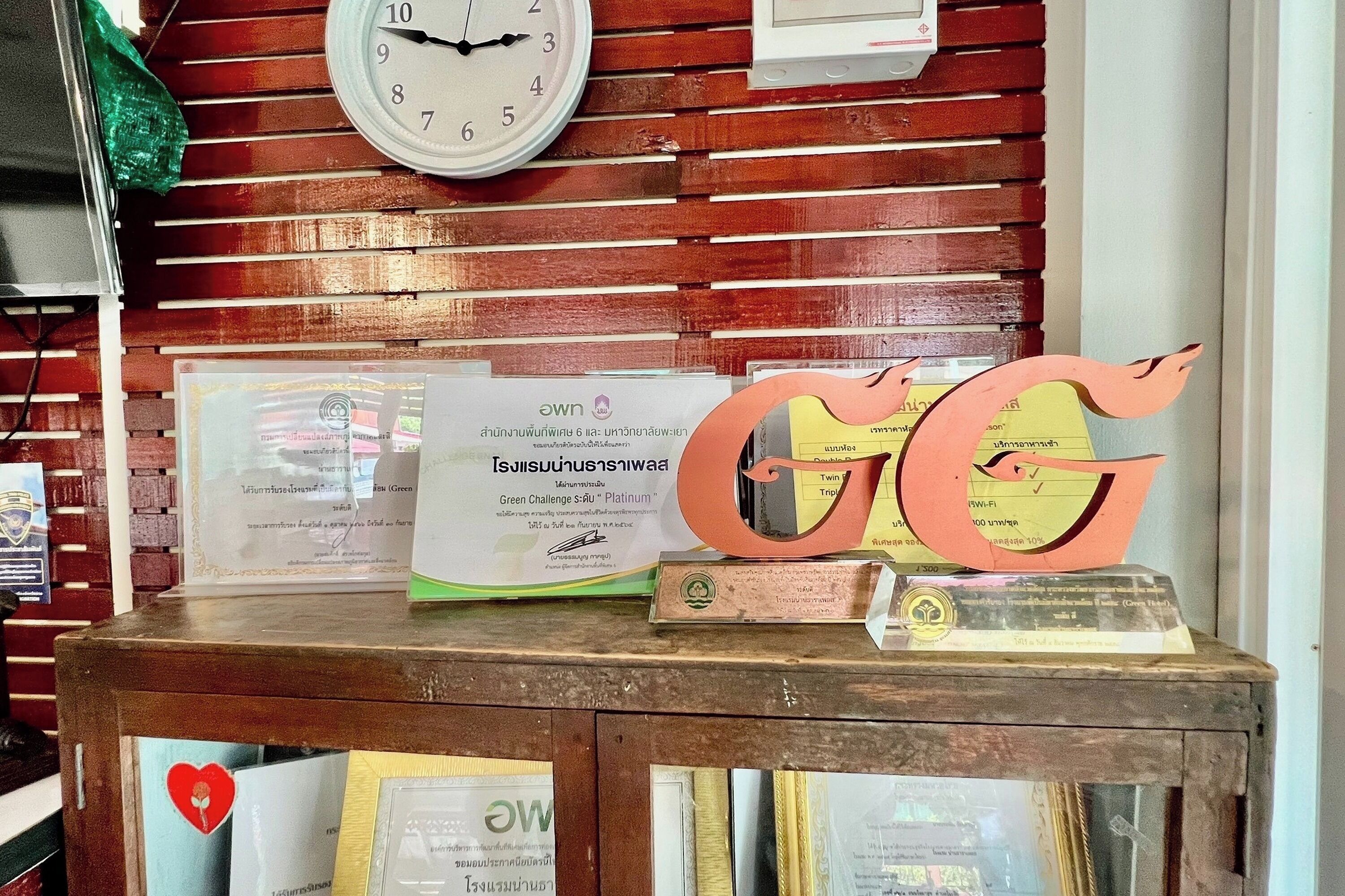 Una mesa de exhibición de madera con diplomas, un reloj y un letrero decorativo con las iniciales 'GG'.