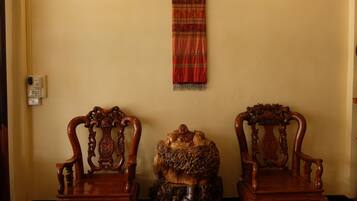 Two ornate wooden chairs with intricate carvings, a decorative wooden sculpture, and a red patterned tapestry hanging on the wall.