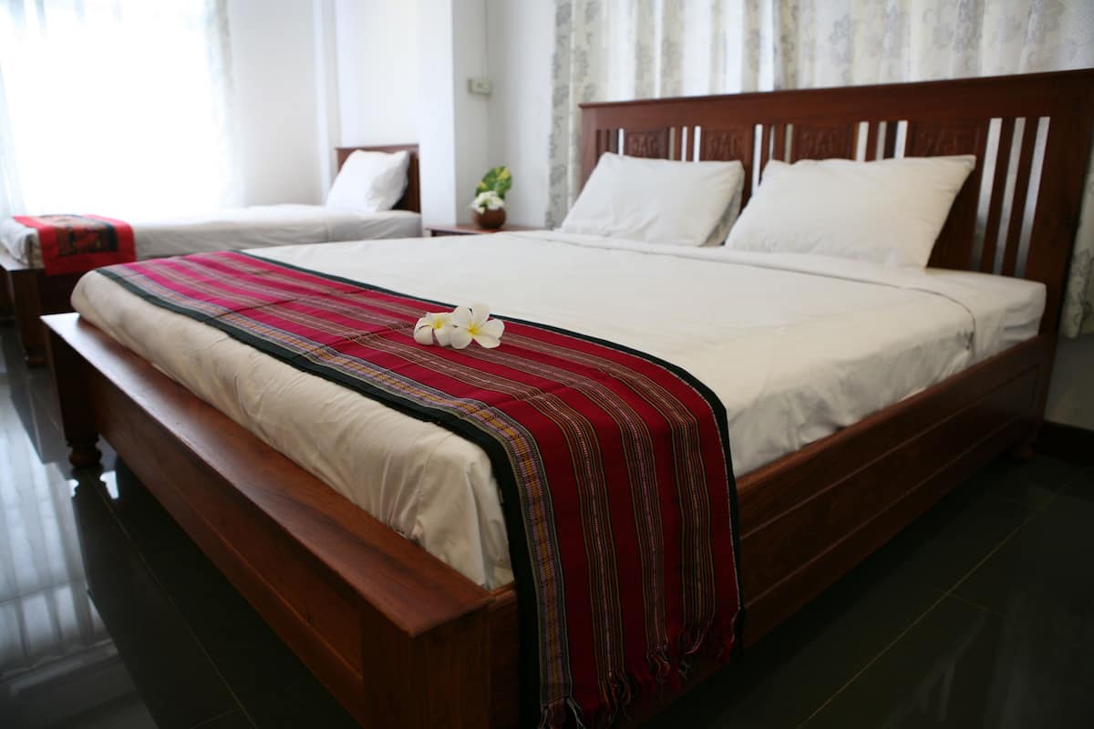 A hotel room with a large bed, a wooden headboard, and a red and black striped blanket.
