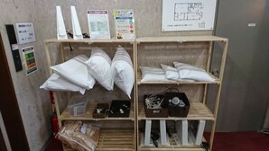 A room with shelves displaying pillows, a fire extinguisher, and a floor plan on the wall. - Hotel Muroran Hills (Muroran)