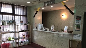 A reception area with a counter, a computer, and a chair. There are shelves with various items and a sign on the wall. - Hotel Muroran Hills (Muroran)