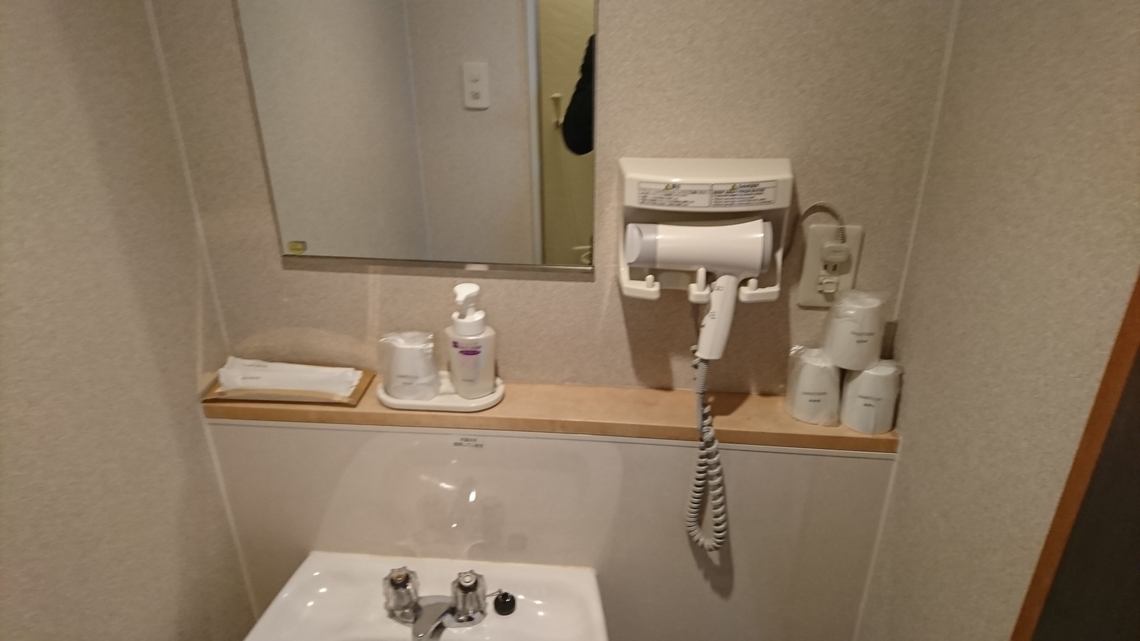 Ein Badezimmer mit Waschbecken, Spiegel, Fön und Toilettenartikeln.