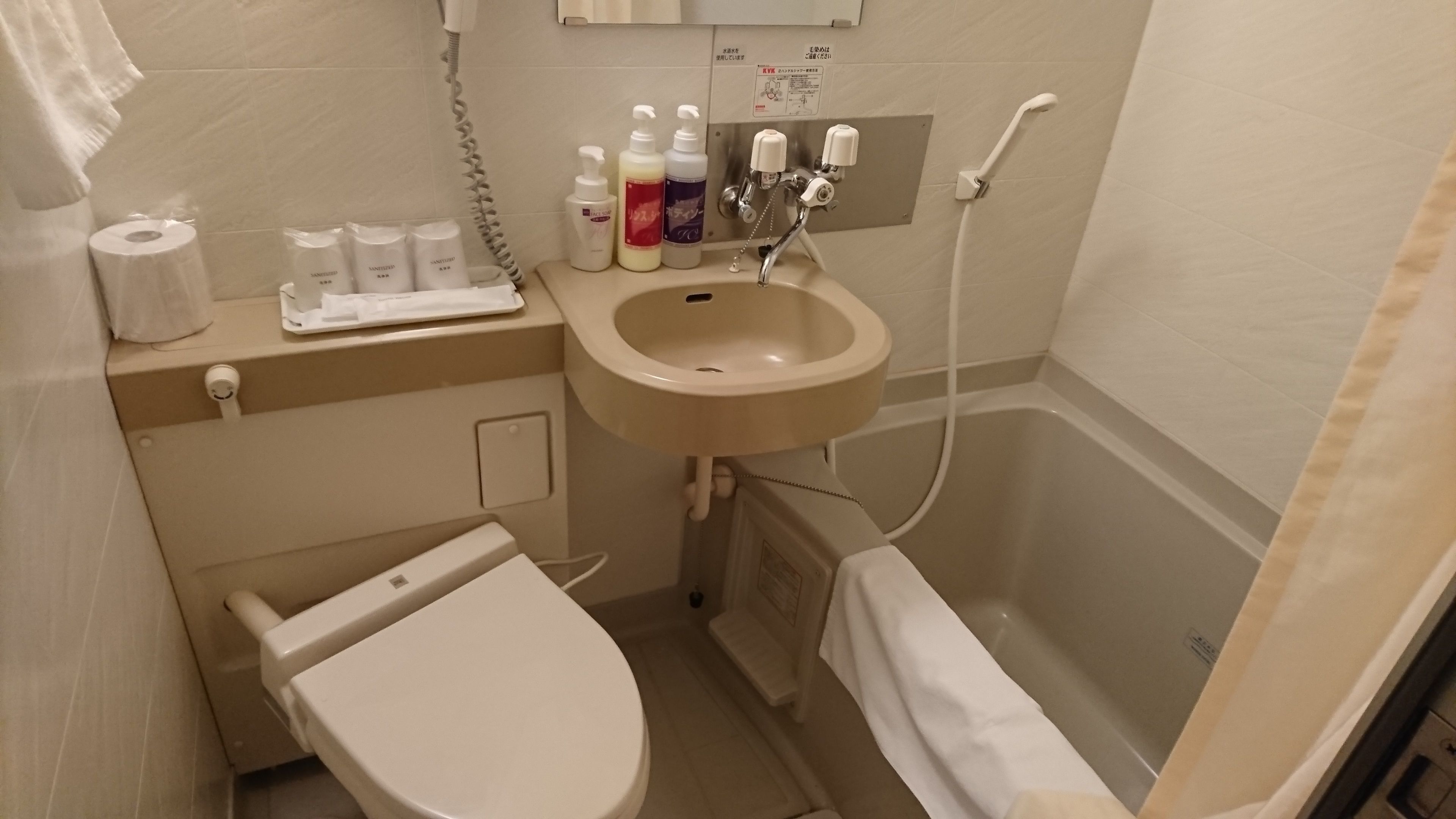 Un baño pequeño con inodoro, lavabo y ducha. Hay artículos de aseo sobre el mostrador.