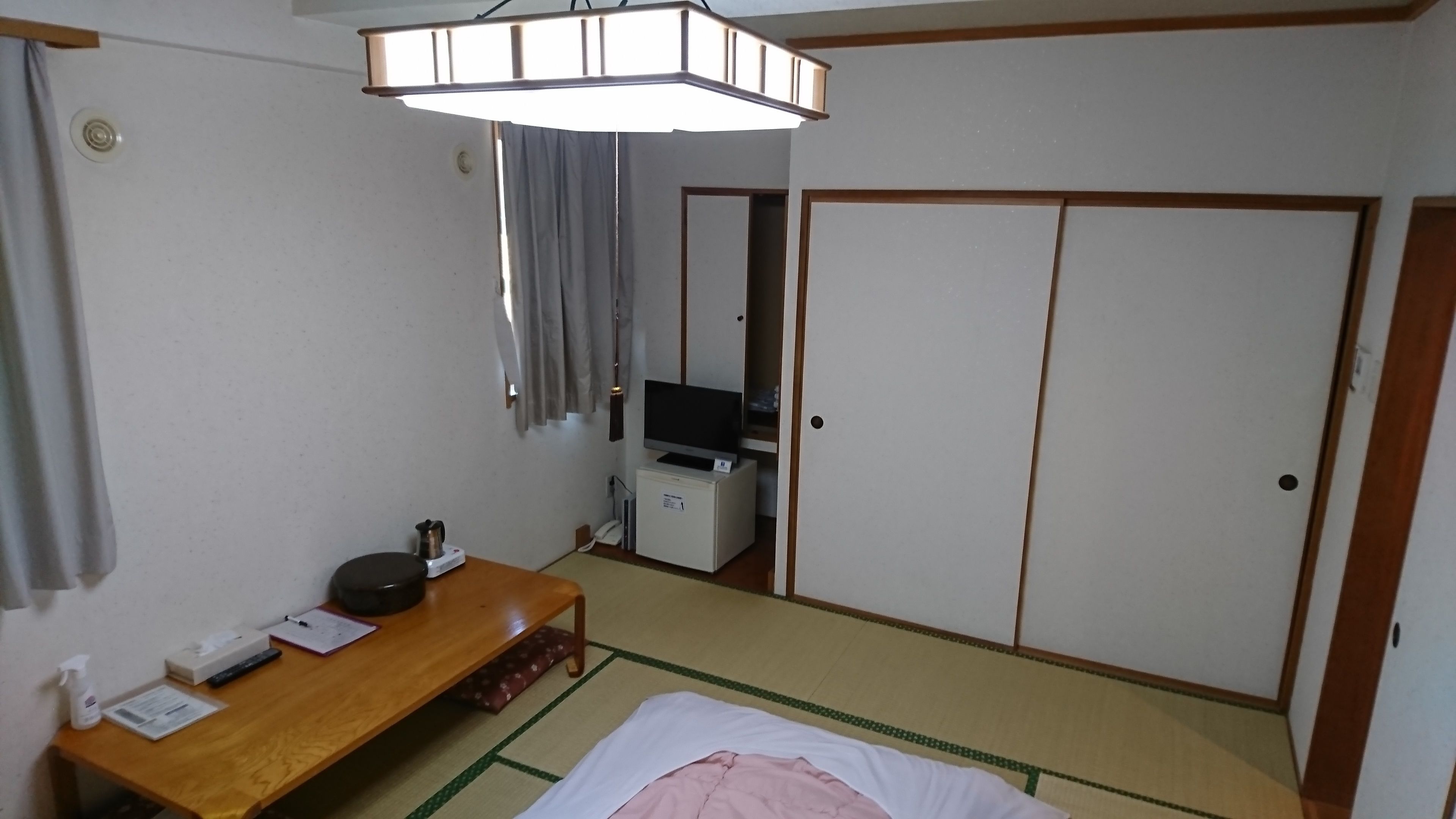 A hotel room with a bed, a desk with a kettle, a television on a small cabinet, and a wardrobe.