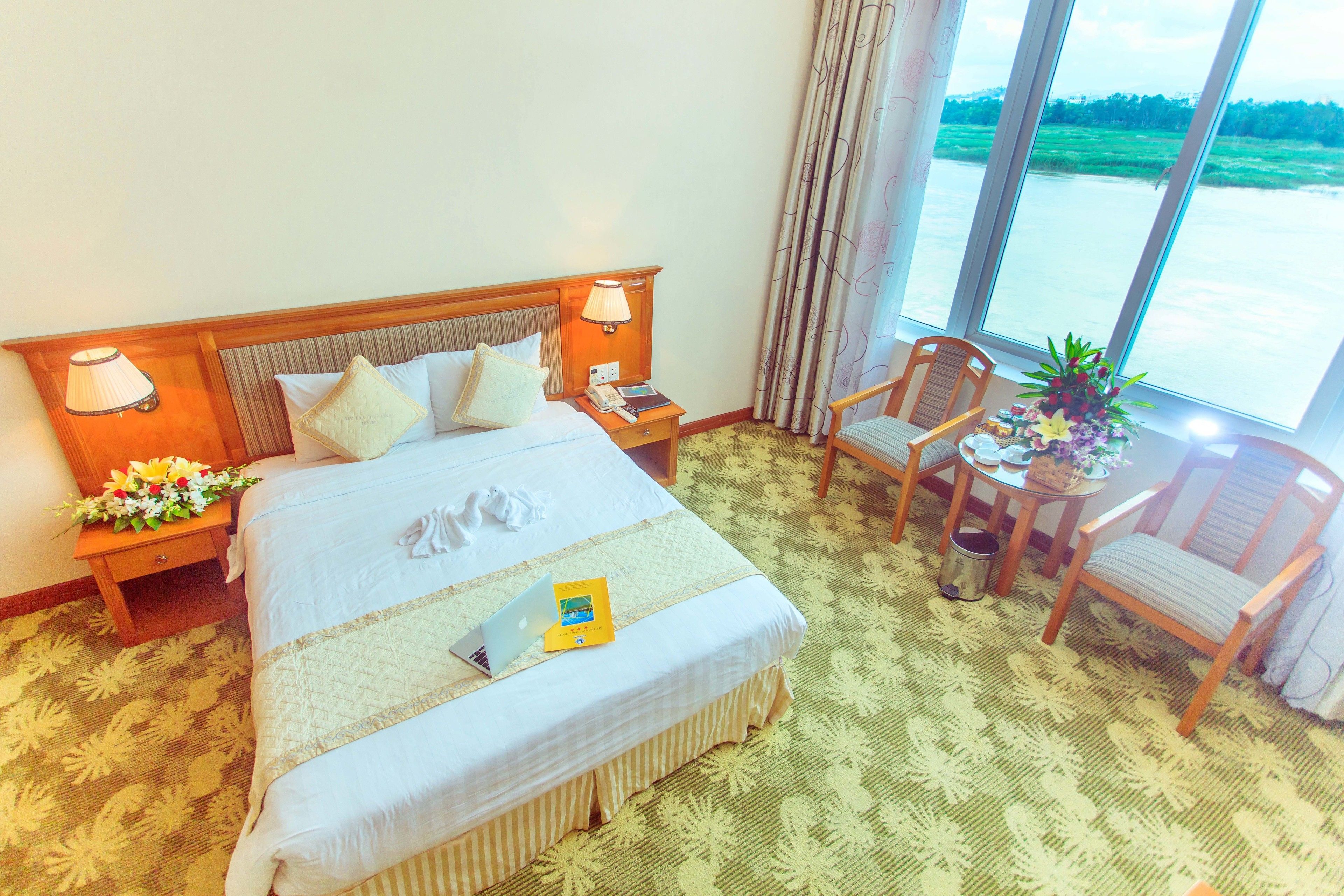 Une chambre d’hôtel avec un grand lit, deux tables de chevet, un bureau avec une chaise et une vue sur une étendue d’eau grâce à de grandes fenêtres.