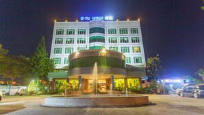 Un hotel con una fontana al centro, un ingresso ben illuminato e un cartello con la scritta “MYTRA RIVERSIDE HOTEL”.