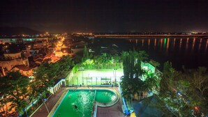 Vista notturna di una zona piscina con edifici circostanti e un ponte sullo sfondo.