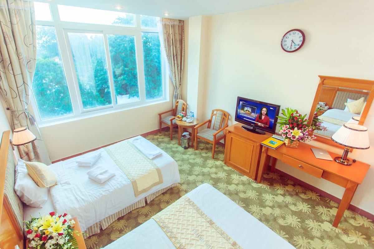Una habitación de hotel con una cama, un escritorio con computadora, un televisor y un reloj en la pared.