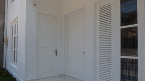 A white exterior of a house with two closed doors and a window with shutters.