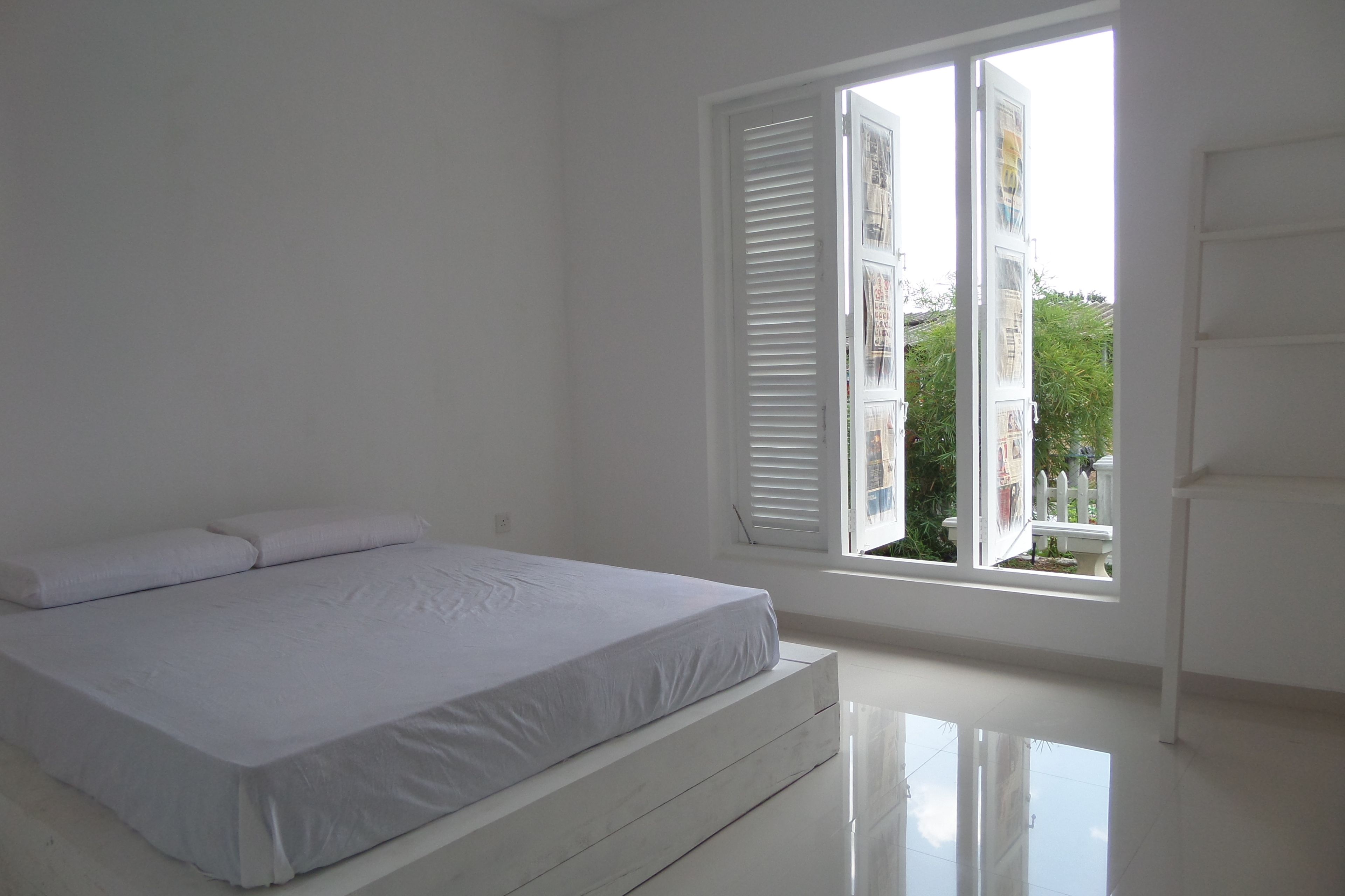 Un dormitorio con cama, paredes blancas y una ventana con persianas.