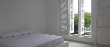 Un dormitorio con cama, paredes blancas y una ventana con persianas.