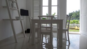 A room with a white desk, a chair, a television on the wall, and a window with blinds.