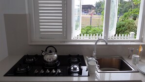 A kitchen with a gas stove, kettle, sink, and window with blinds.