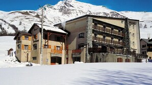 A hotel with a stone facade, multiple balconies, and a mountain backdrop. - Les Agneaux (Villar-d'Arene)