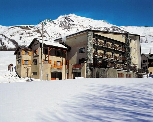 A hotel with a stone facade, multiple balconies, and a mountain backdrop.
