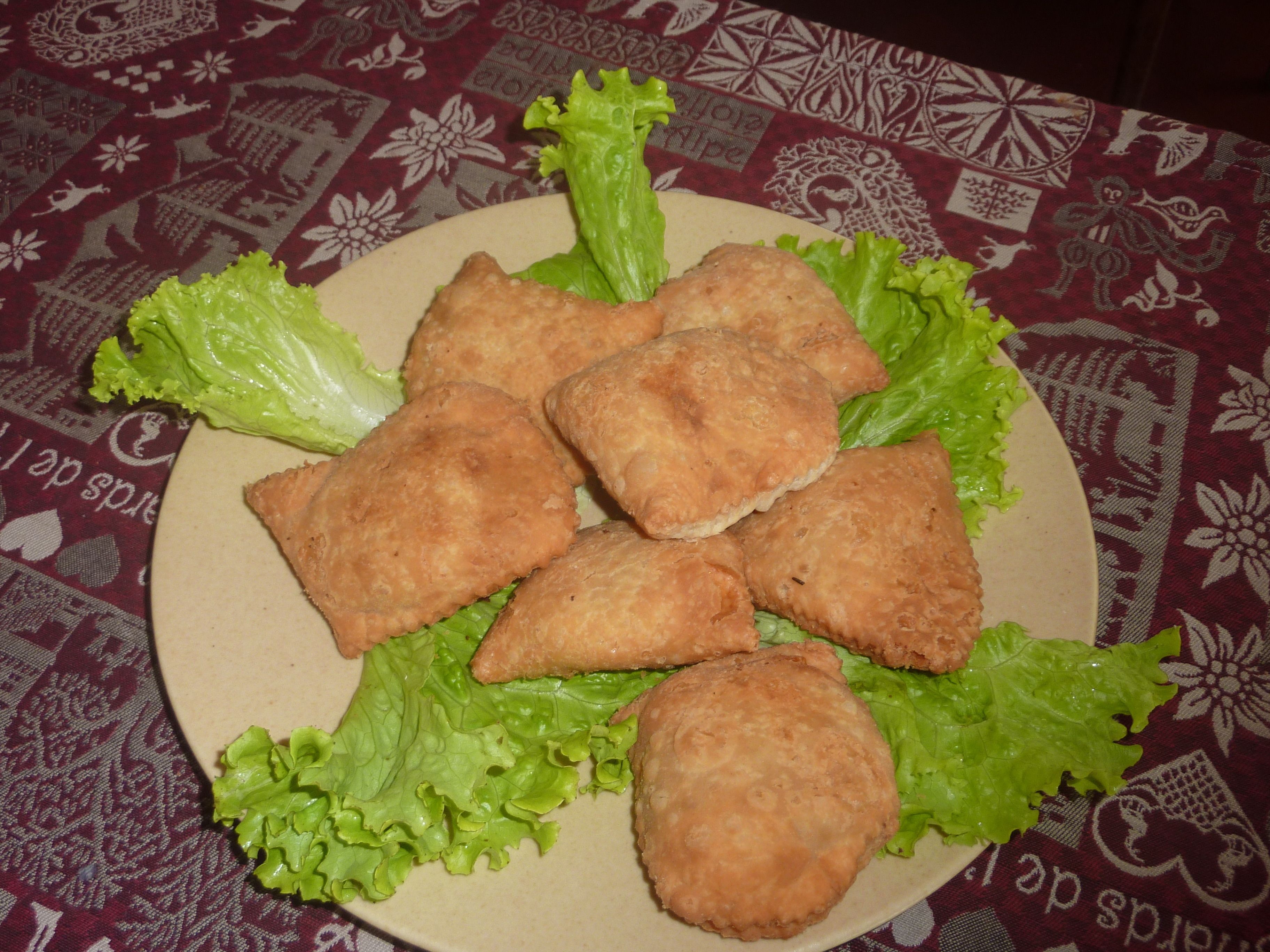 Une assiette de plats frits est posée sur une table recouverte d’une nappe à motifs.