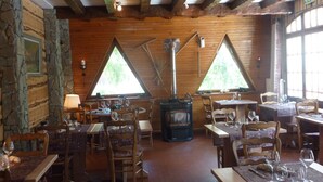 A rustic dining area with wooden tables and chairs, stone walls, and large triangular windows allowing natural light. - Les Agneaux (Villar-d'Arene)
