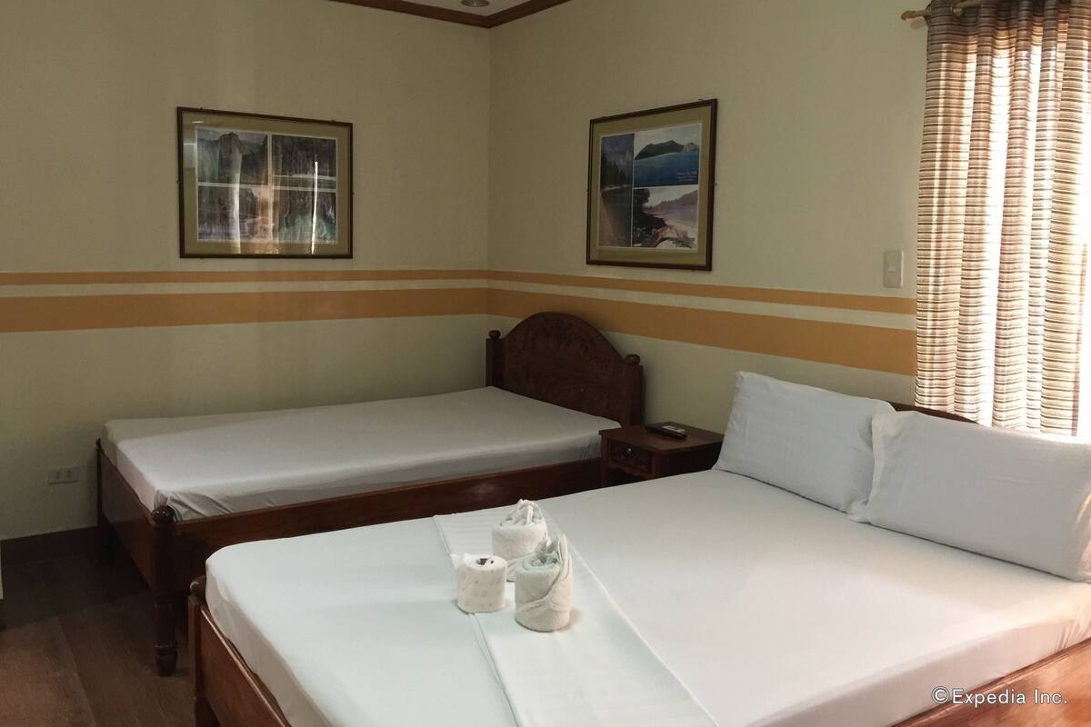 A hotel room with two single beds, a wooden headboard, a nightstand, and two framed pictures on the walls.