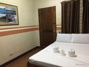 A hotel room with a bed, a wooden door, a framed photo on the wall, and a curtain. - Islands View Inn (Coron)