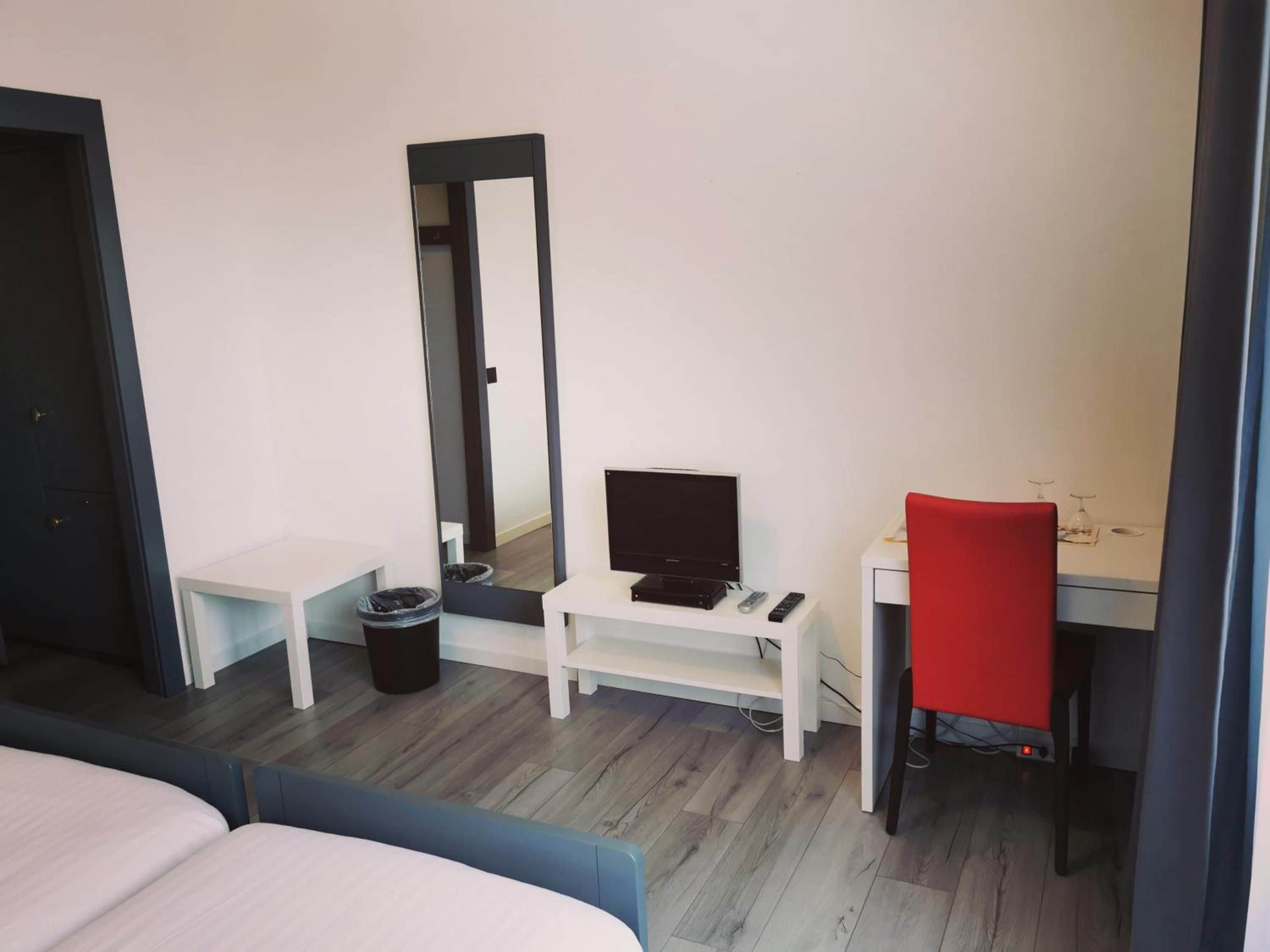 Camera d'albergo con un letto, una scrivania con un computer, una sedia, uno specchio e un cestino.