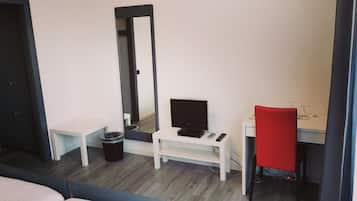 A hotel room with a bed, a desk with a computer, a chair, a mirror, and a trash bin.