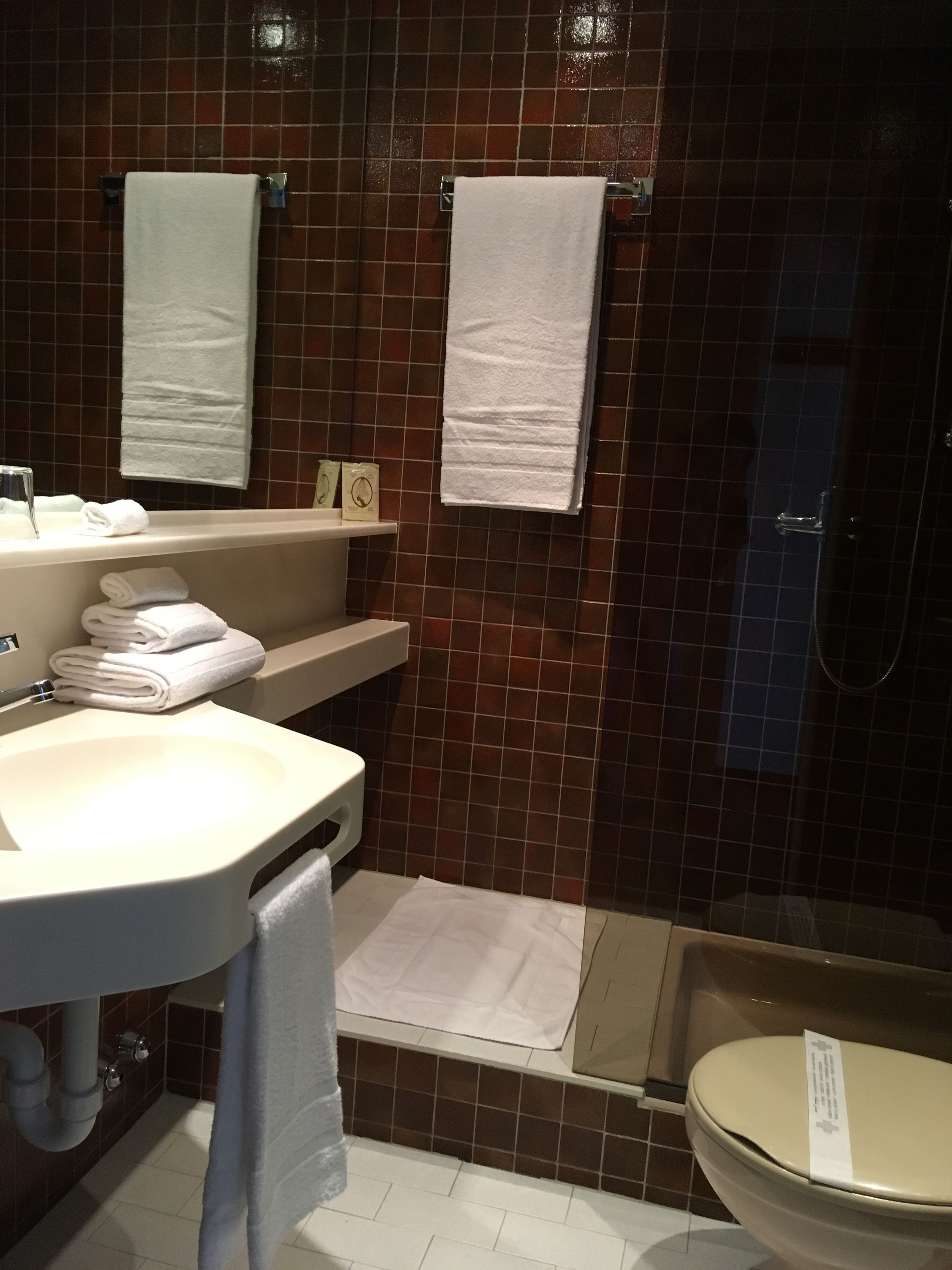 Une salle de bain avec un lavabo, un miroir et des toilettes. On y trouve des serviettes et des articles de toilette sur le comptoir.