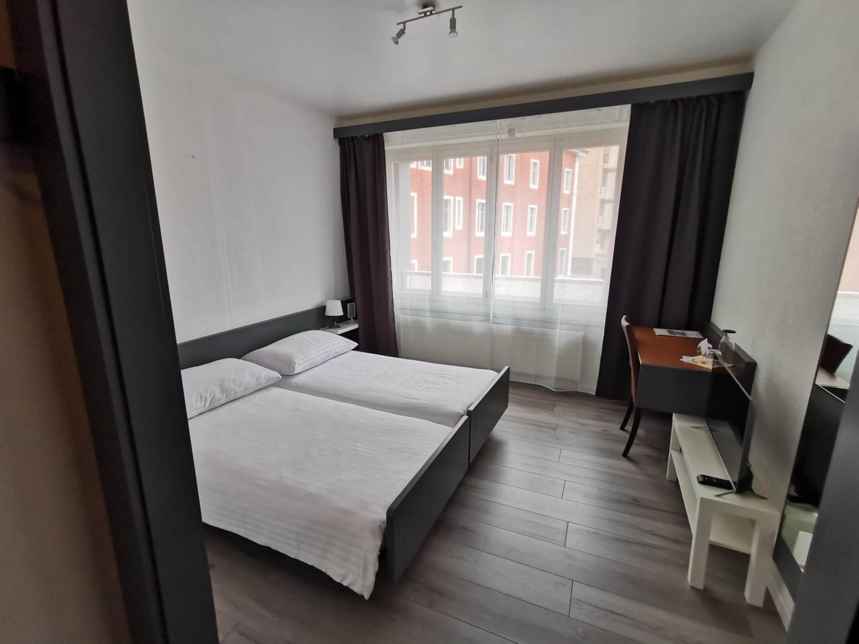 Ein Hotelzimmer mit einem Bett, einem Schreibtisch und Blick auf Gebäude durch das Fenster.