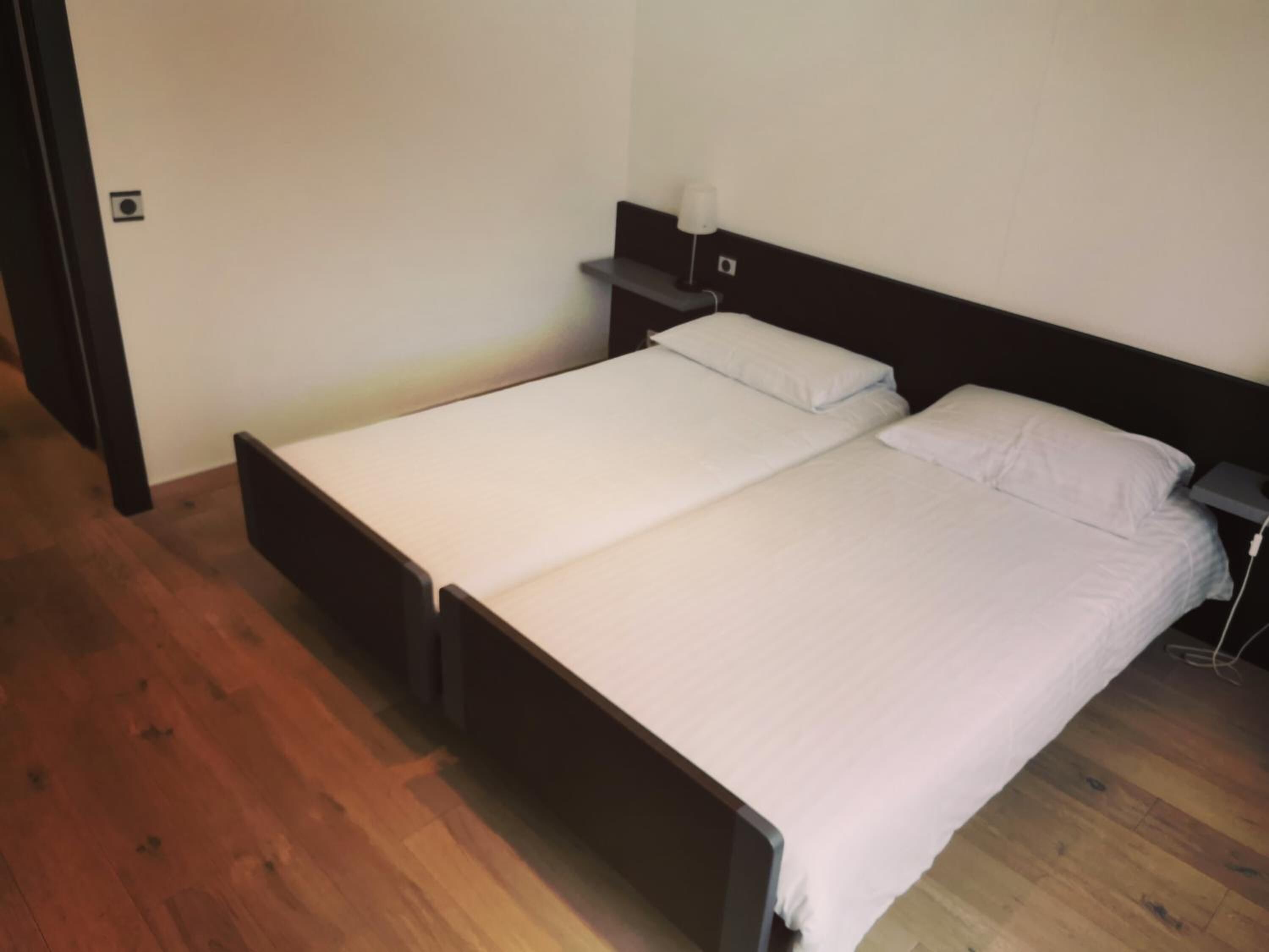 A single bed with a wooden frame and white bedding in a room with wooden flooring and a dark headboard.