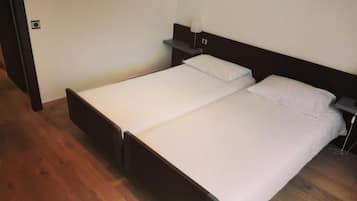 A single bed with a wooden frame and white bedding in a room with wooden flooring and a dark headboard.