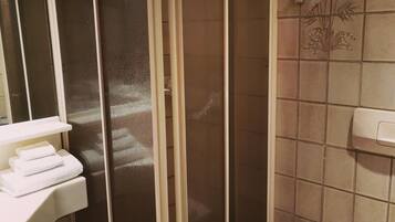 A bathroom with a walk-in shower, a toilet, and a sink with towels.