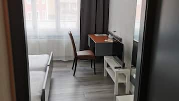 Ein Hotelzimmer mit Bett, Schreibtisch, Stuhl und einem fenster mit Vorhängen.