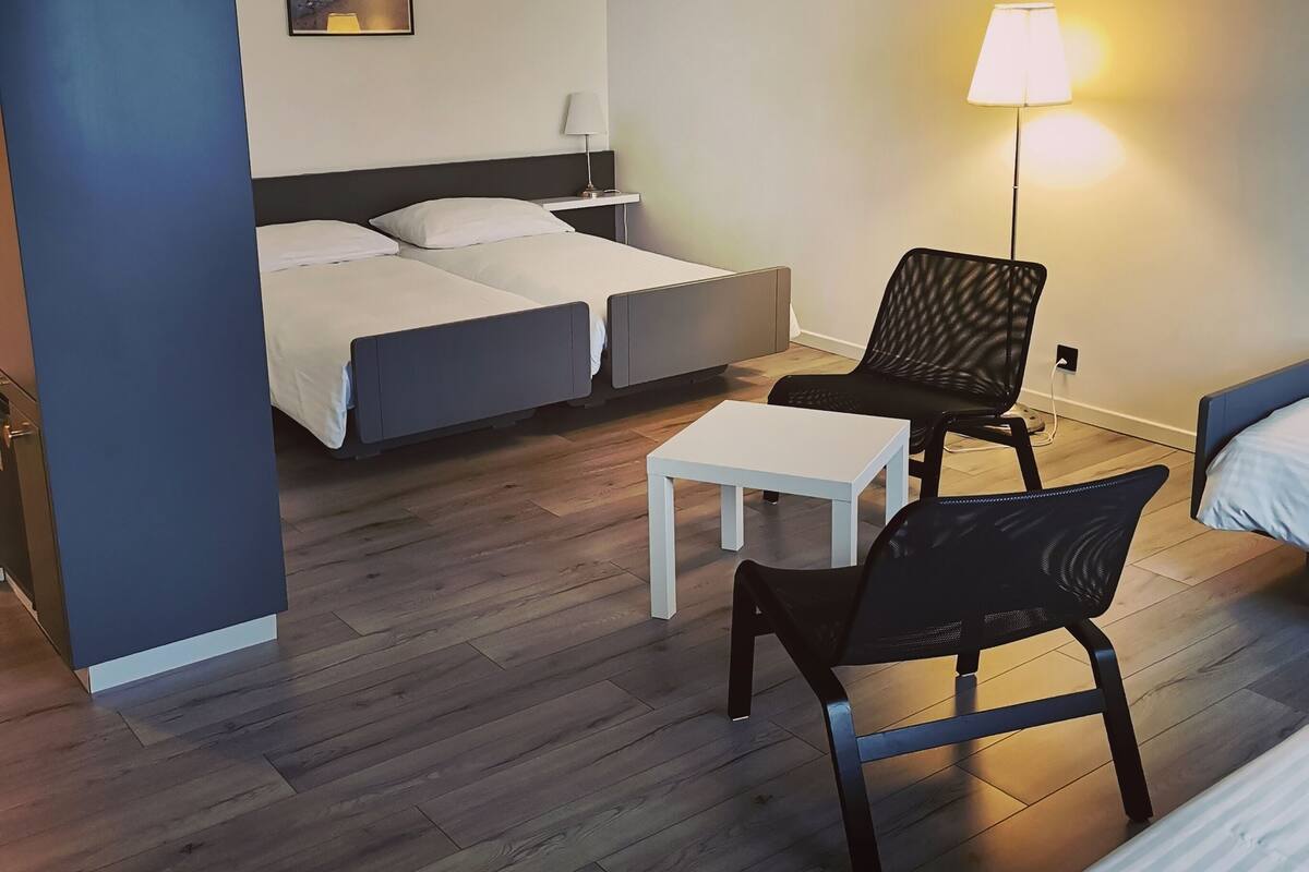 Quarto de hotel moderno com uma cama, uma escrivaninha, uma cadeira e um abajur.