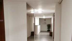 Un couloir avec un mur recouvert de miroirs, un plancher en bois et une plante visible au loin.