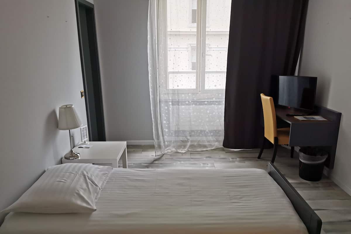 Quarto de hotel com cama, secretária com cadeira, televisão e luminária.