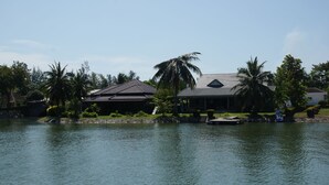 A house by a lake with a boat docked nearby. - Rayong Rental Pool Villas (Klaeng)
