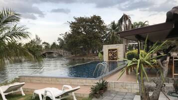 A swimming pool with a stone border, two white lounge chairs, and a small bridge over a water feature.
