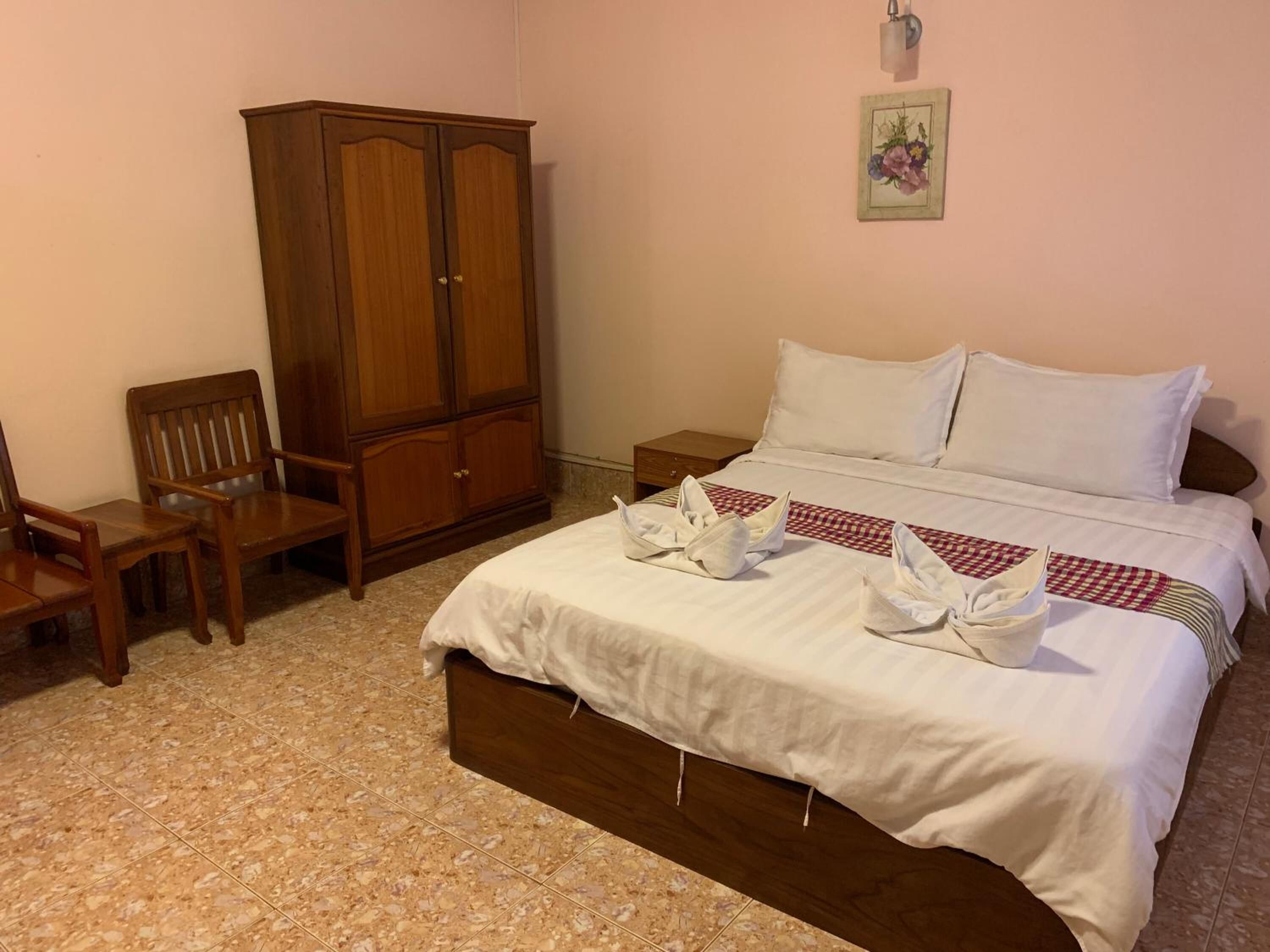 A bedroom with a bed, a wooden wardrobe, a chair, and a nightstand.