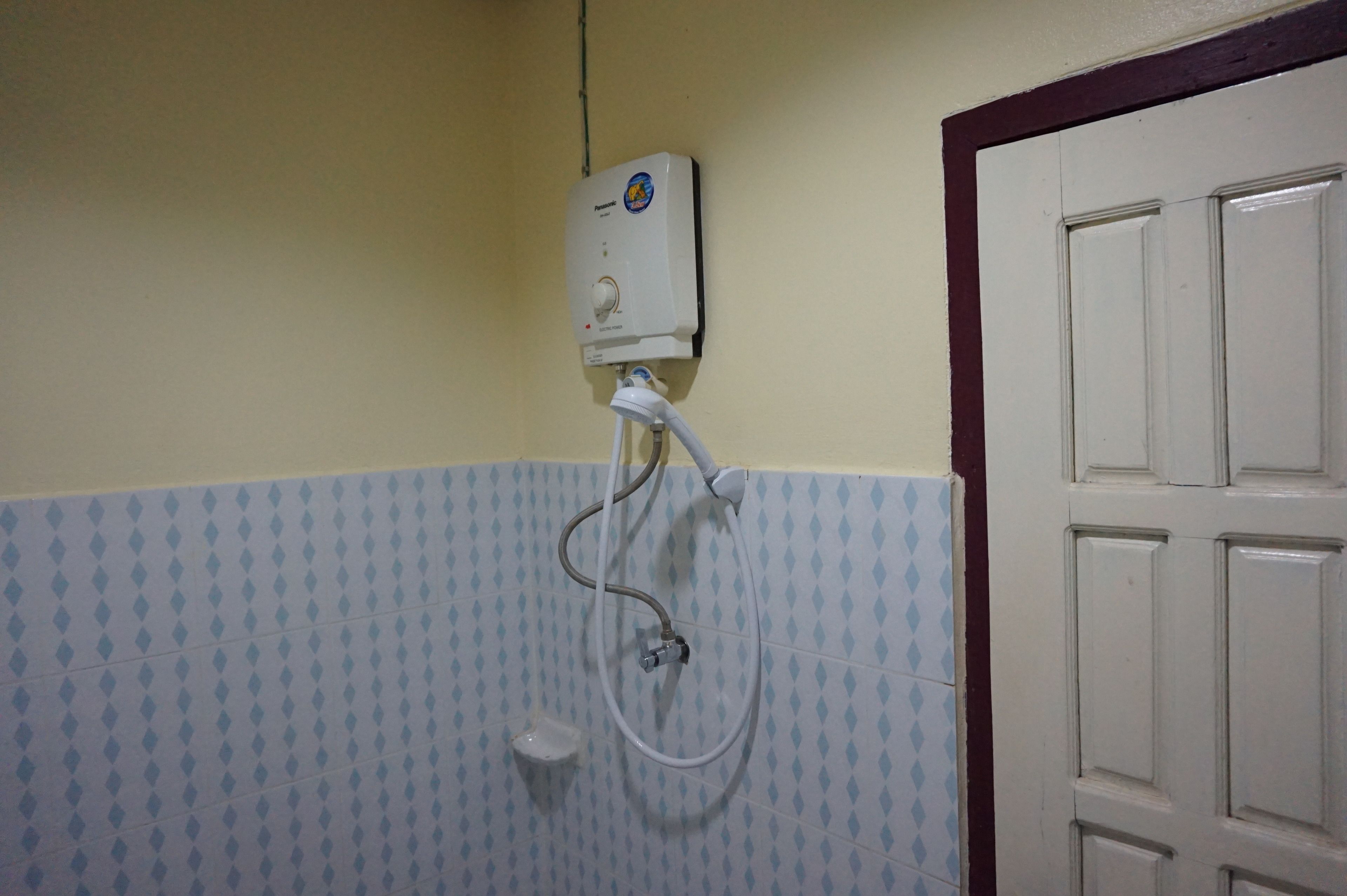 A bathroom with a wall-mounted water heater, a showerhead, and a white door.