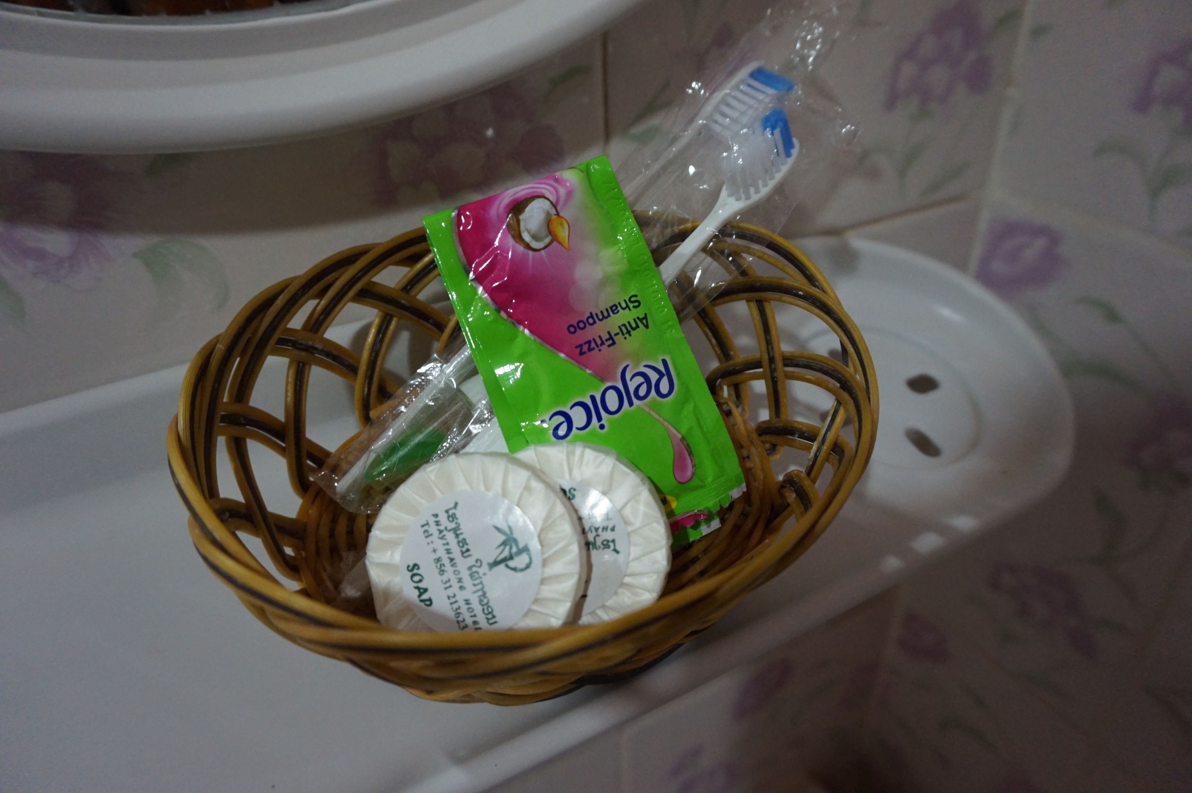 A wicker basket containing a shampoo bottle, a toothbrush, and a soap bar on a bathroom sink.